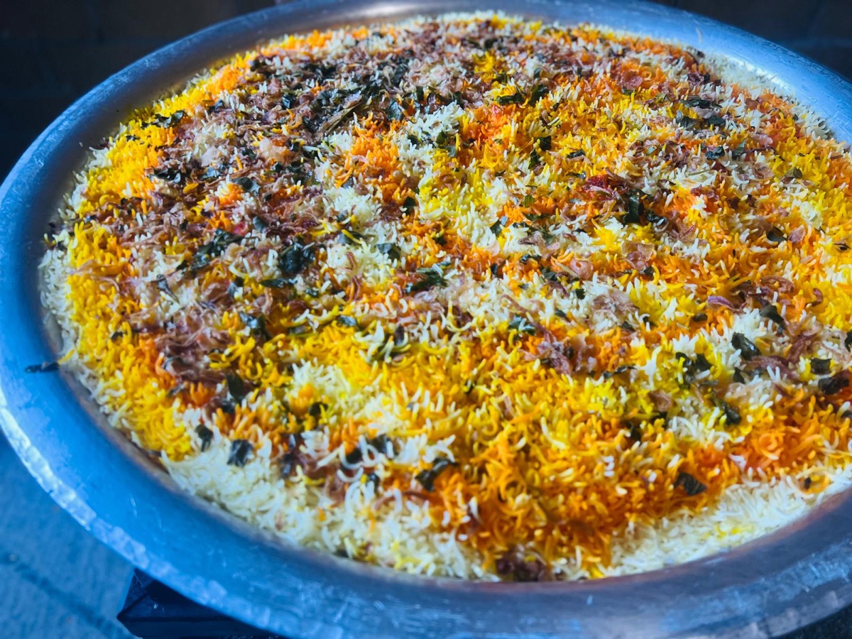 Close-up of a full catering tray of biryani garnished with fried onions and mint